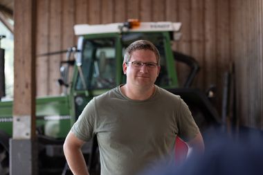 Ein Landwirt steht in einer Scheune vor seinem Trecker.