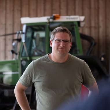 Ein Landwirt steht in einer Scheune vor seinem Trecker.