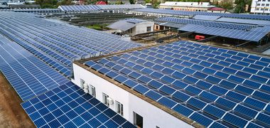 Eine Luftaufnahme von Industriehallen und Parkplätzen, die komplett mit Solarpaneelen bedeckt sind.
