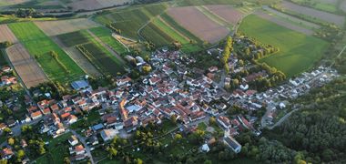Lauftaufnahme eines kleinen Dorfes inmitten von grünen Feldern.