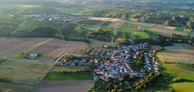 Lauftaufnahme eines kleinen Dorfes inmitten von grünen Feldern.