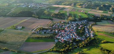 Lauftaufnahme eines kleinen Dorfes inmitten von grünen Feldern.