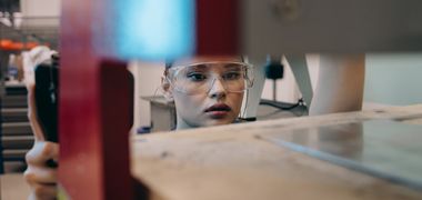 Eine Handwerkerin mit Schutzbrille richtet eine Platte aus.