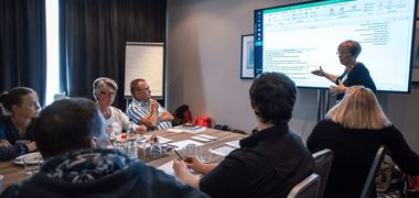 Eine Frau präsentiert in einem Konferenzraum etwas an einem großen Monitor.