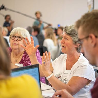 Eine ältere Frau erzählt und gestikuliert bei einer Bürgerrat Veranstaltung.