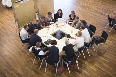 Eine Kleingruppe eines Bürgerrates diskutiert, Kärtchen liegen auf den Tischen und hängen an den Flipcharts.