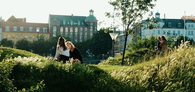 Zwei junge Frauen sitzen in der Abendsonne im Stadtpark inmitten von Sommergräsern..