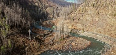Vertrocknete Bäume säumen braungebrannte Hänge, in der Mitte ein Fluss.