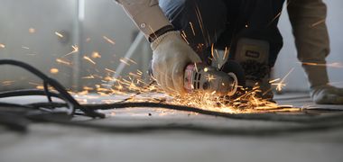 Ein Handwerker flext Metall, Funken fliegen.