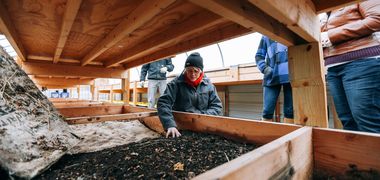 Eine Frau prüft die Zusammensetzung von Erde in einem Holzkasten.