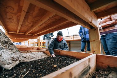 Eine Frau prüft die Zusammensetzung von Erde in einem Holzkasten.