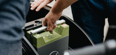 Ein Mensch greift nach einer herausnehmbaren Batterie von einem Elektroroller.