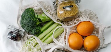 Gemüse liegt in Stoff-Netztaschen auf einem Tisch. Wiederverwendbare Gläser sind mit Hülsenfrüchten gefüllt und beschriftet.