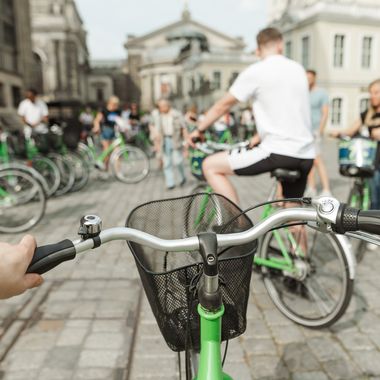 Sicht eines Fahrradfahrers auf sein grünes Leihfahrrad, im Hintergrund mehr Menschen auf grünen Rädern.