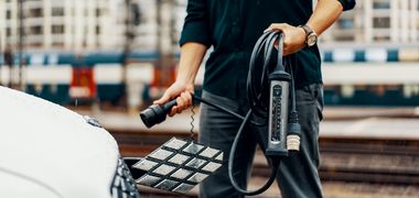 Ein Mensch hält ein langes Ladekabel und Stecker vor einem Elektroauto.