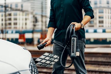 Ein Mensch hält ein langes Ladekabel und Stecker vor einem Elektroauto.