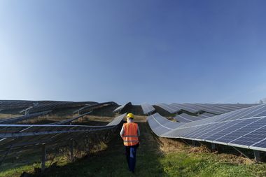 Ein Arbeiter läuft durch einen Solarpark. Zur Linken und Rechten mehrere Reihen Solarpanele.