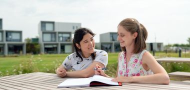 Zwei Frauen sitzen draußen an einem Tisch und schauen in ein Heft.