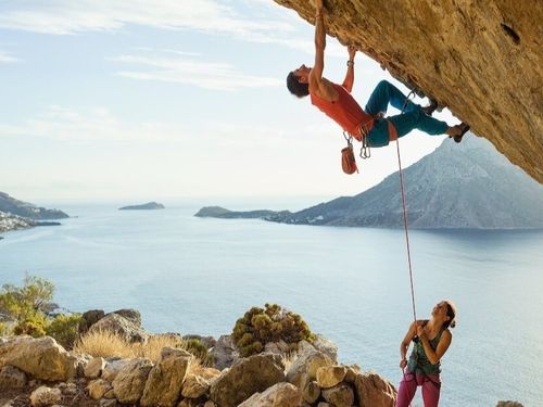 A young man starts climbing in a cave entrance while his female partner secures him.