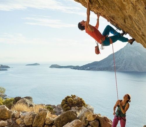 A young man starts climbing in a cave entrance while his female partner secures him.