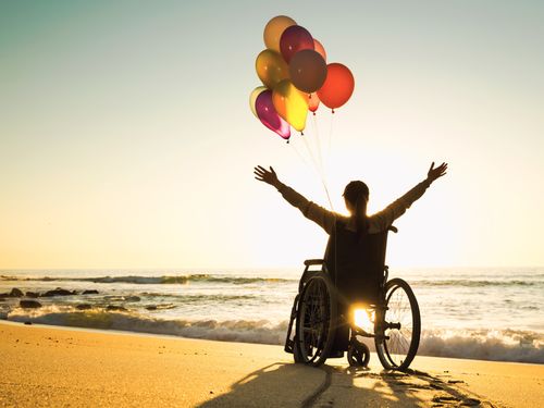 Euphoric person in a wheelchair with balloons on the beach