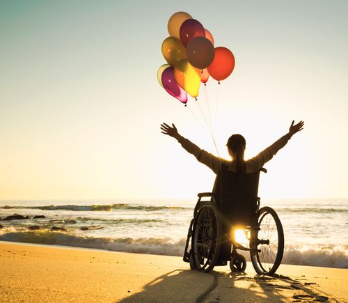 Euphoric person in a wheelchair with balloons on the beach