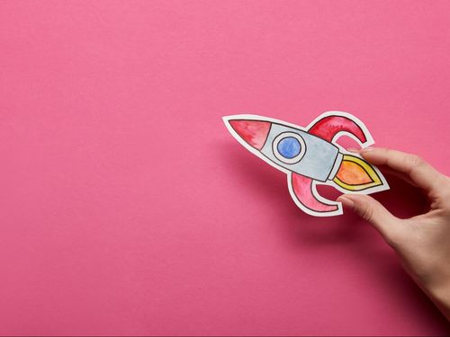 top-view-of-hand-holding-rocket-on-pink-background-2022-12-16-19-32-39-utc