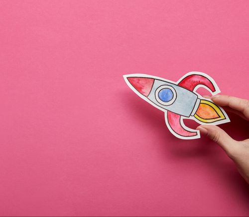 top-view-of-hand-holding-rocket-on-pink-background-2022-12-16-19-32-39-utc