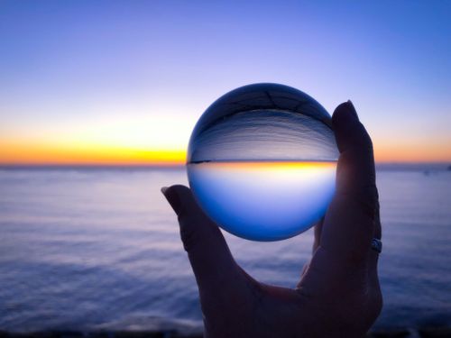 Woman holding a crystal ball, looking to inverted beautiful dawn seascape at sunrise