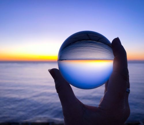 Woman holding a crystal ball, looking to inverted beautiful dawn seascape at sunrise