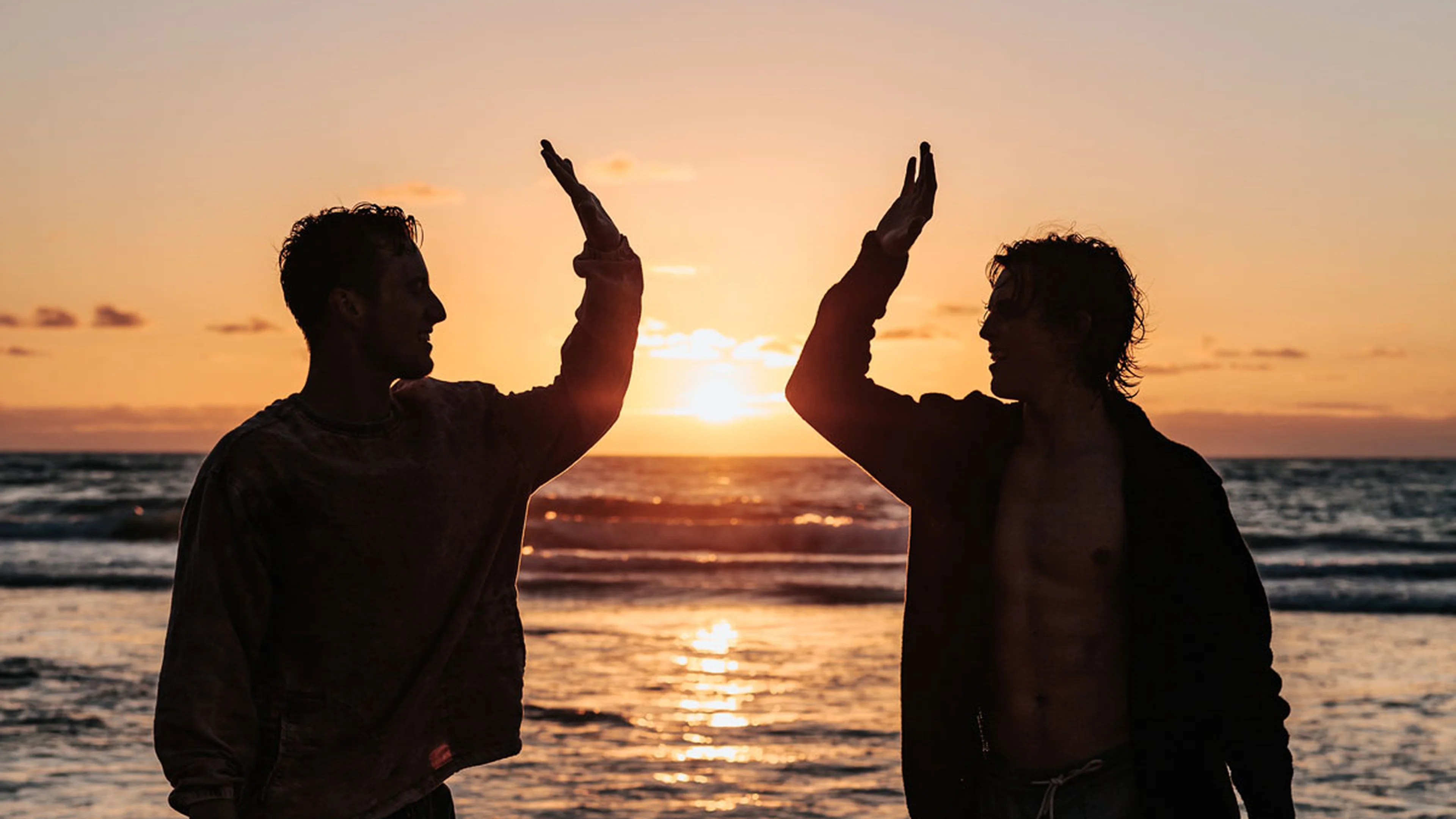 Two silhouetted figures at sunset on the beach high fiving