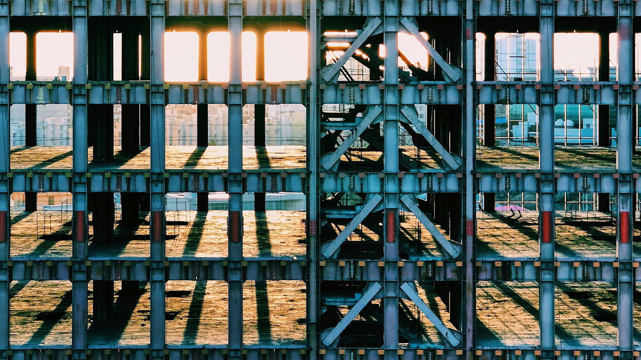 Sunlight casting shadows through the skeletal frame of a building under construction.