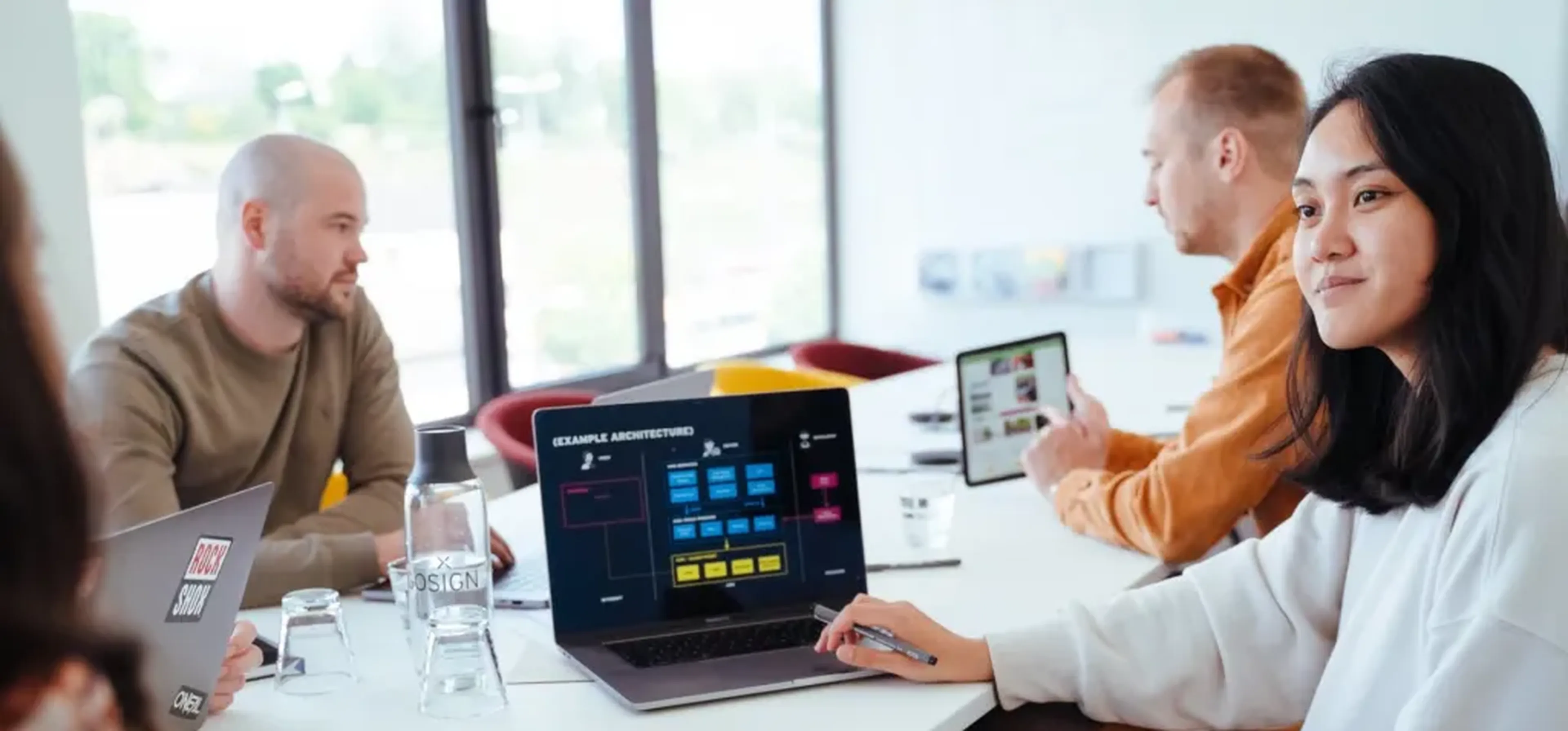 Zwei Frauen und zwei Männer sitzen an einem Tisch und arbeiten an ihren Laptops.