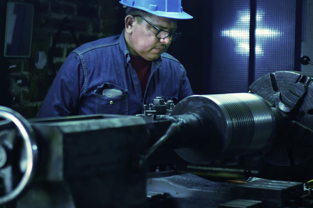Mann in Arbeitskleidung mit blauem Helm vor einer Maschine.