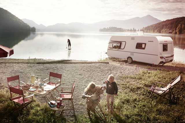 Dethleffs Wohnwagen an einem Bergsee, daneben sind Mutter und Kind.