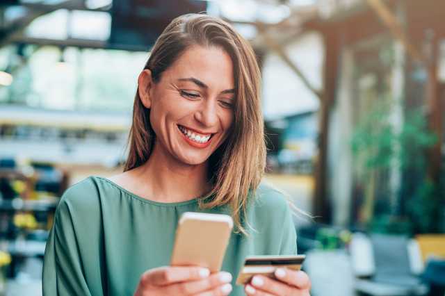 Glückliche Frau gibt ihre Kreditkartendaten in ihr Smartphone ein.
