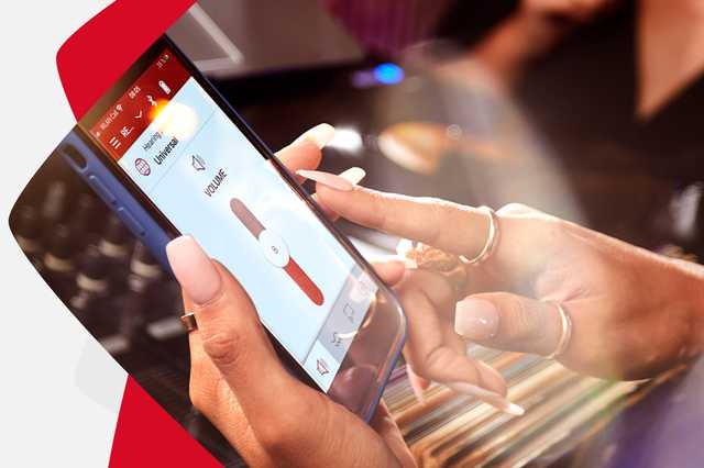 A person with manicured nails uses a smartphone app to adjust the volume. The screen displays a red and white interface with volume control.