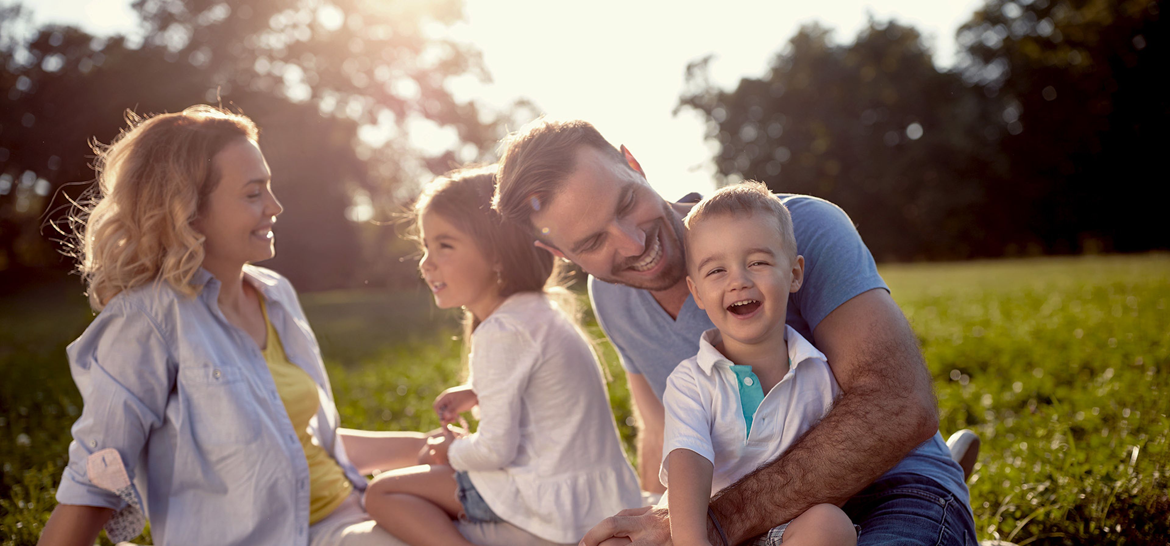 Eine glückliche Familie sitzt auf einer Picknickdecke in der Sonne auf einer Wiese.