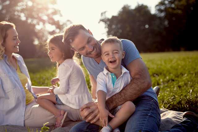 Eine glückliche Familie sitzt auf einer Picknickdecke in der Sonne auf einer Wiese.