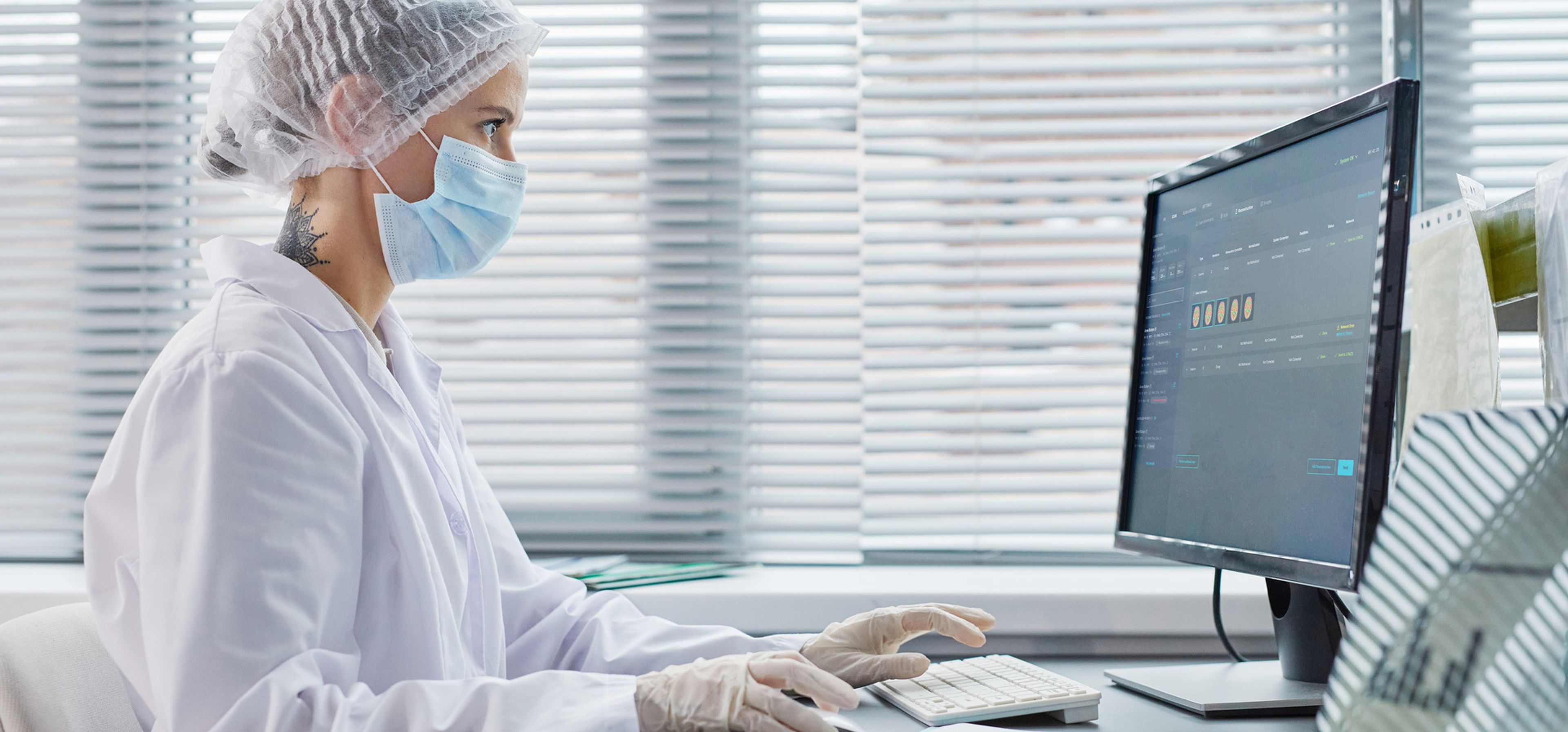 Wissenschaftliche Fachkraft mit Haarnetz, Maske und Handschuhen arbeitet am Computer