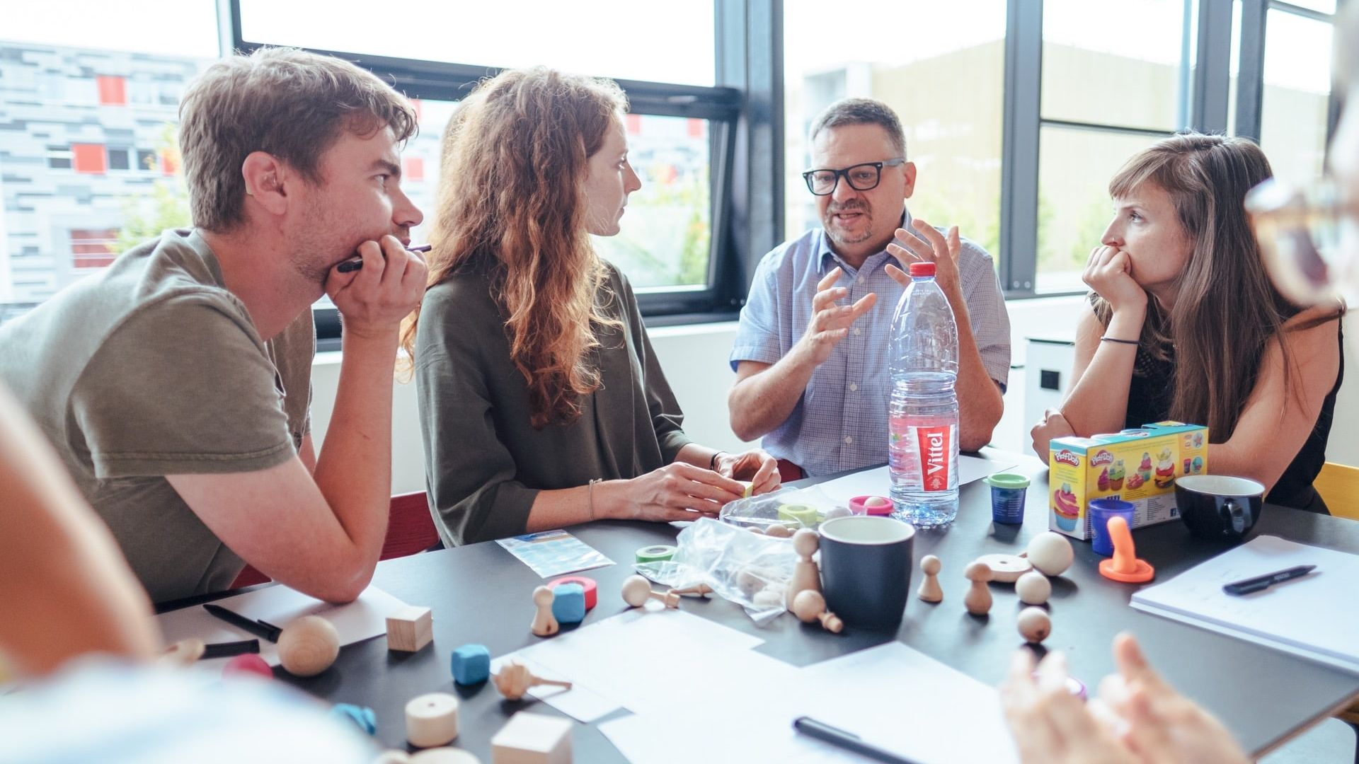 Ein Gruppe steht um einen Tisch und ein Mann erklärt etwas zu Collaborative UX Design.