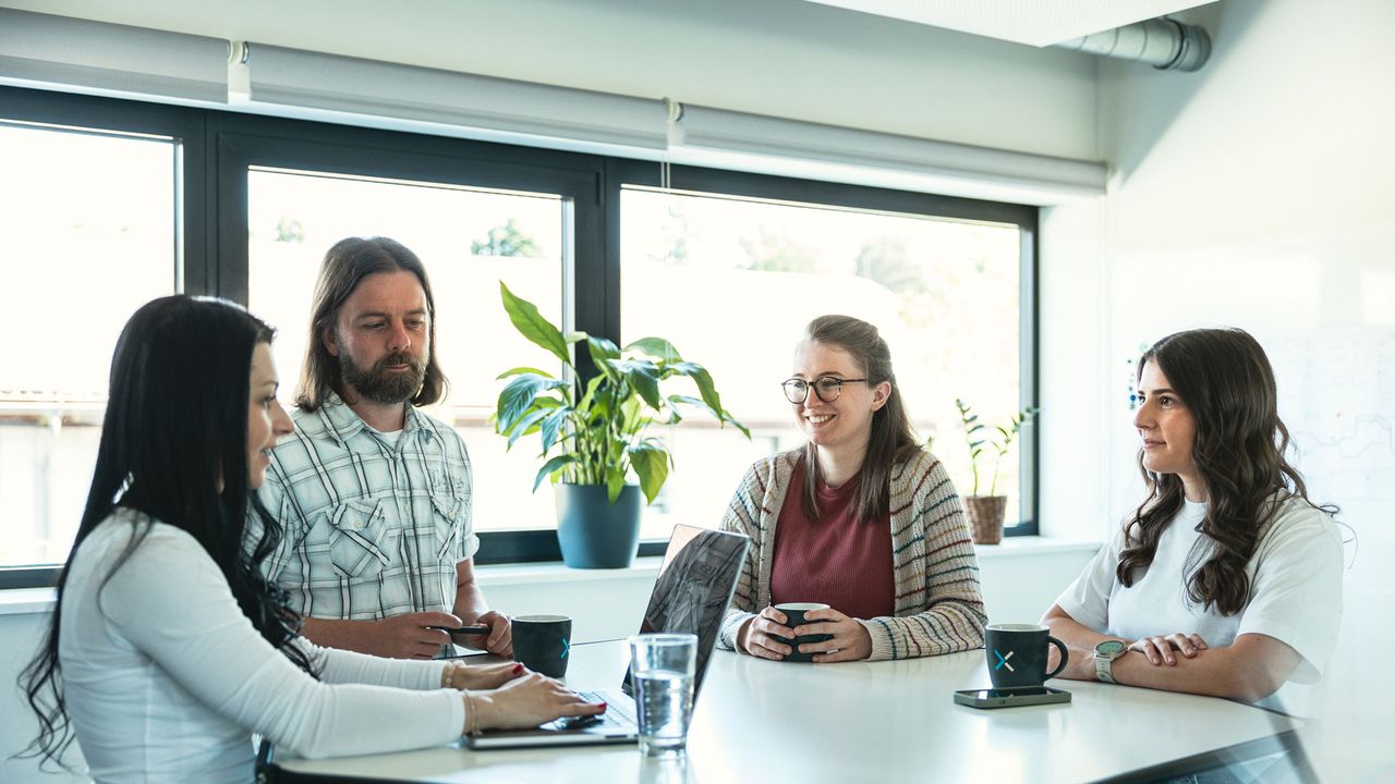 Vier Personen sitzen um einen Tisch in einem Büro und unterhalten sich.