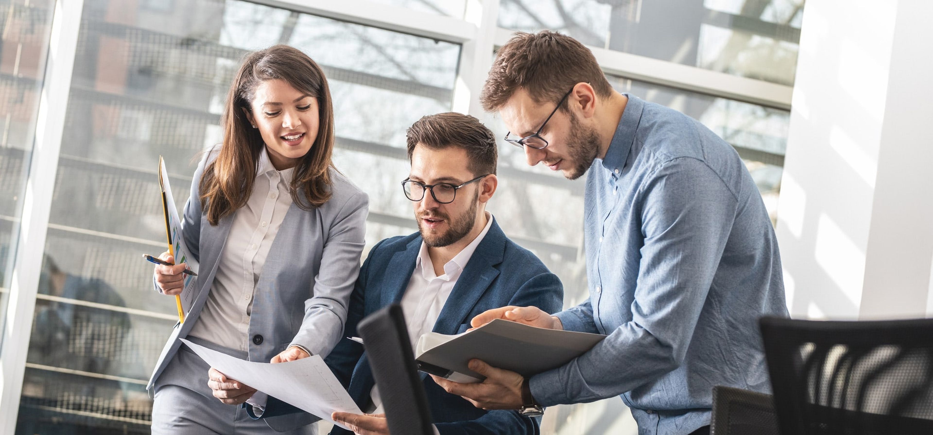 Zwei Männer und eine Frau im Büro diskutieren über Akten.