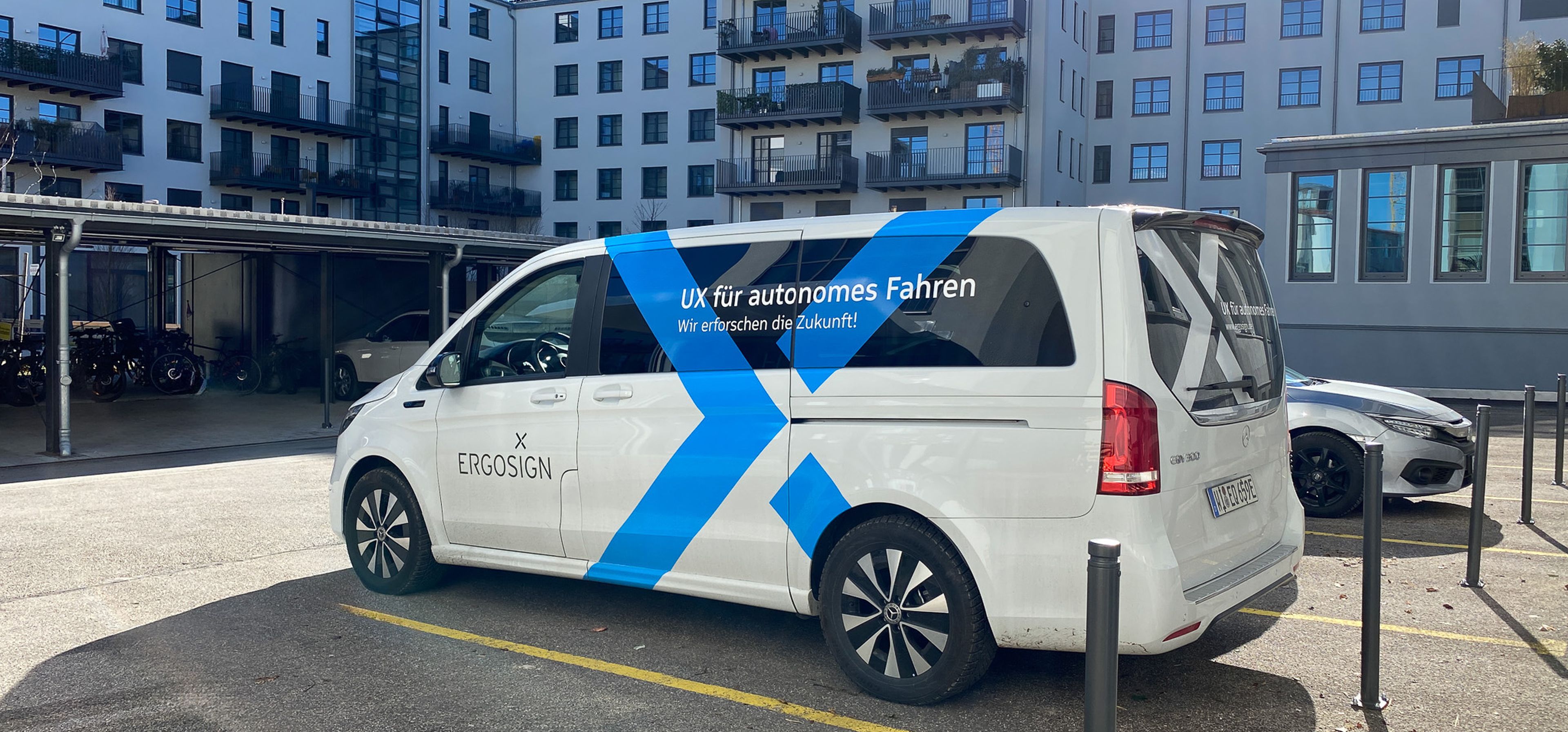 Ein weißer Mercedes Mini-Van mit dem blauen Ergosign Logo, der auf einem Parkplatz steht. parked in a courtyard.