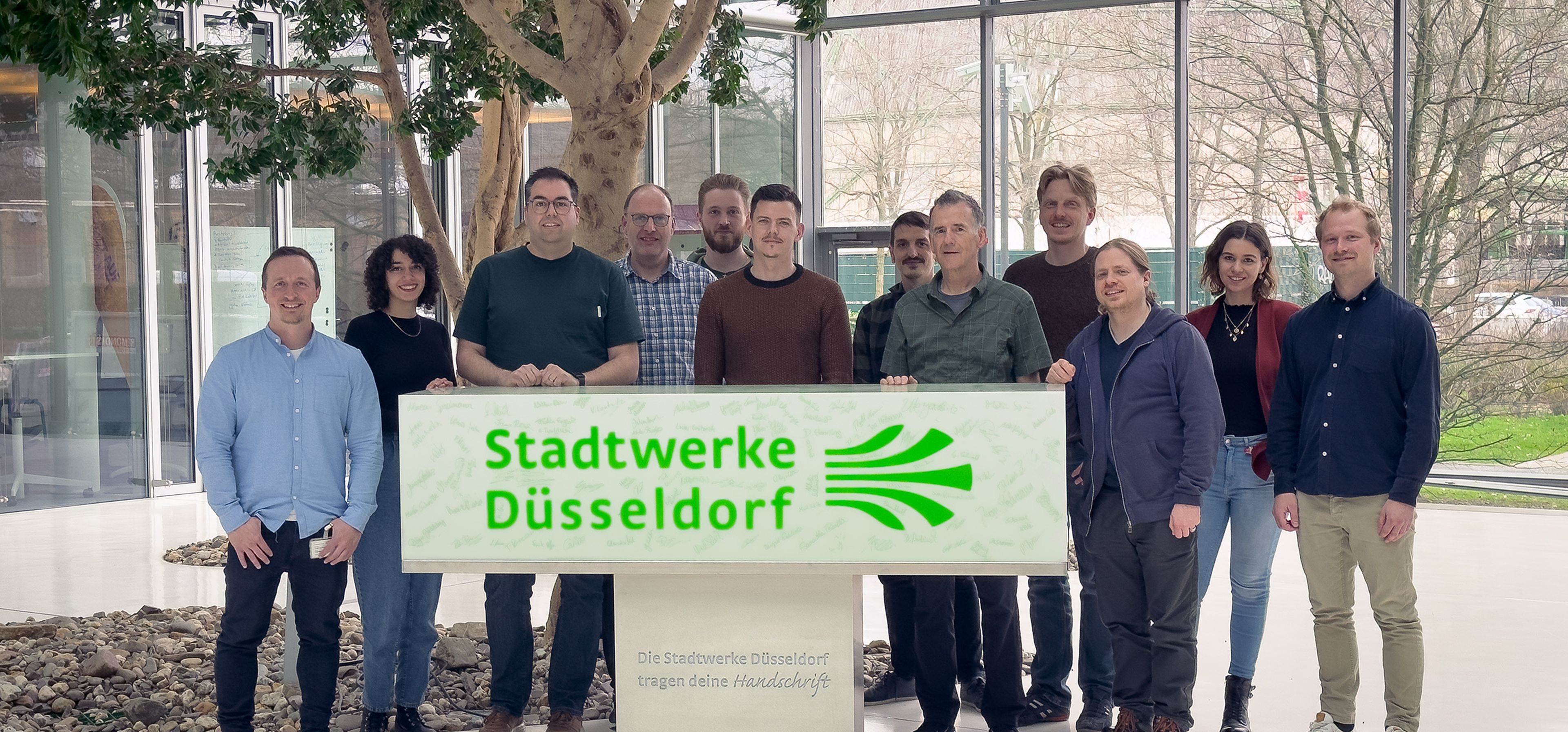 Mitarbeiter der Stadtwerke Düsseldorf und von Ergosign stehen gemeinsam hinter einem Schild der Stadtwerke Düsseldorf