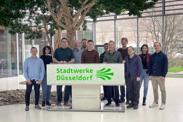Mitarbeiter der Stadtwerke Düsseldorf und von Ergosign stehen gemeinsam hinter einem Schild der Stadtwerke Düsseldorf
