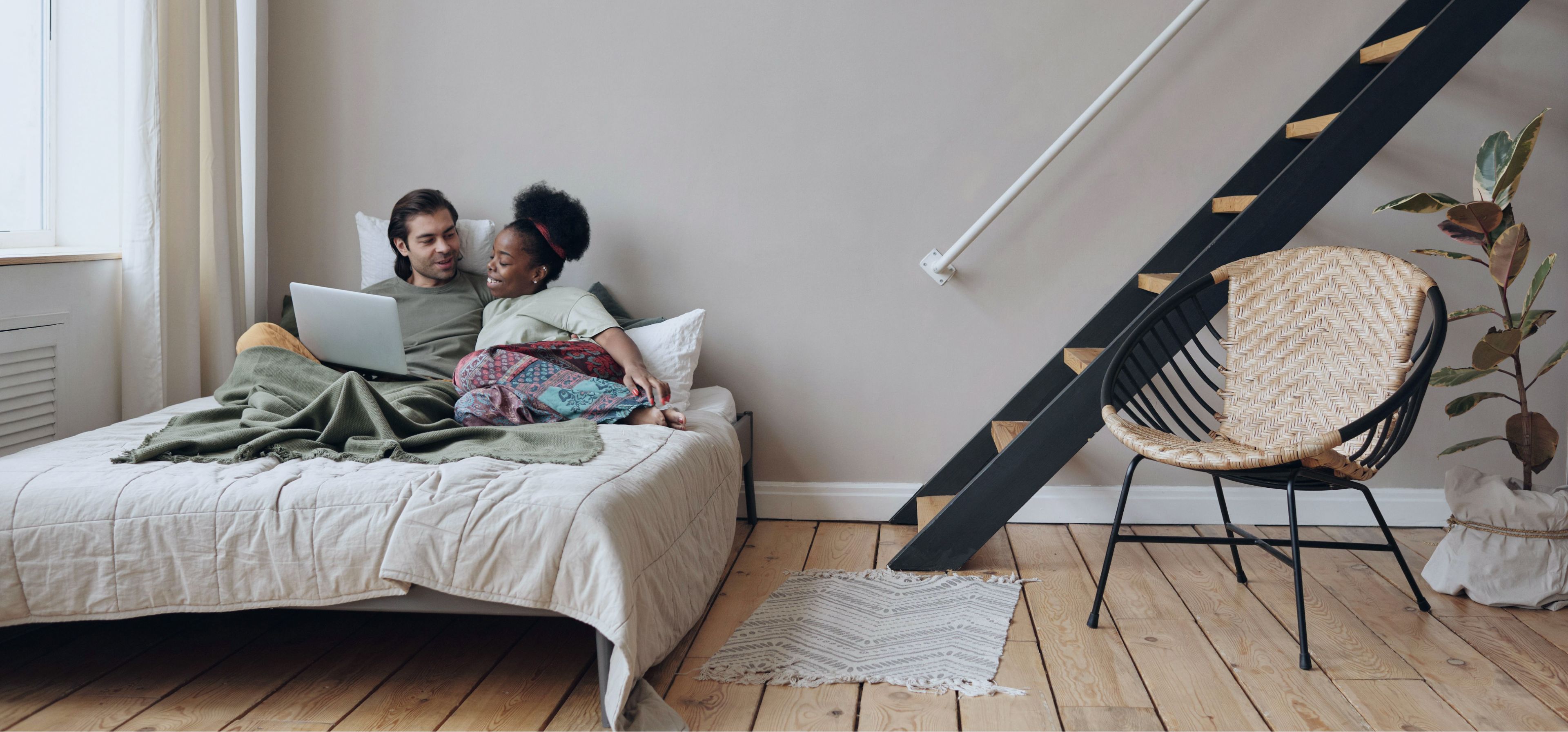 Mann und Frau liegen in einem Bett und schauen lächelnd auf einen Laptop