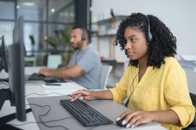 Eine Frau mit Kopfhörern arbeitet konzentriert am Computer.