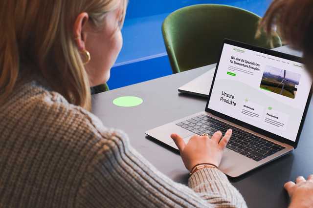 Eine Frau sitzt an ihrem Laptop auf dem die Website der Grünwerke geöffnet ist. Rechts neben ihr sitzt ein Mann, der ebenfalls auf den Bildschirm schaut.