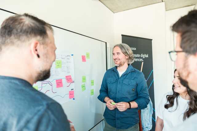 Gruppe von Personen bei der Zusammenarbeit im Büro – sie besprechen Ideen und nutzen Haftnotizen auf einem Whiteboard.